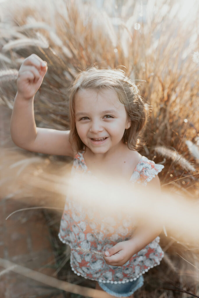 Girl laughing in tall golden grass – family photographer in Bloemendaal