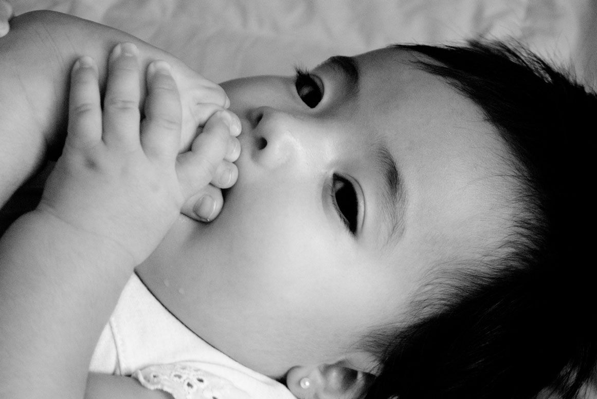 Baby holding their foot to their mouth – documentary newborn photography at home, Haarlem