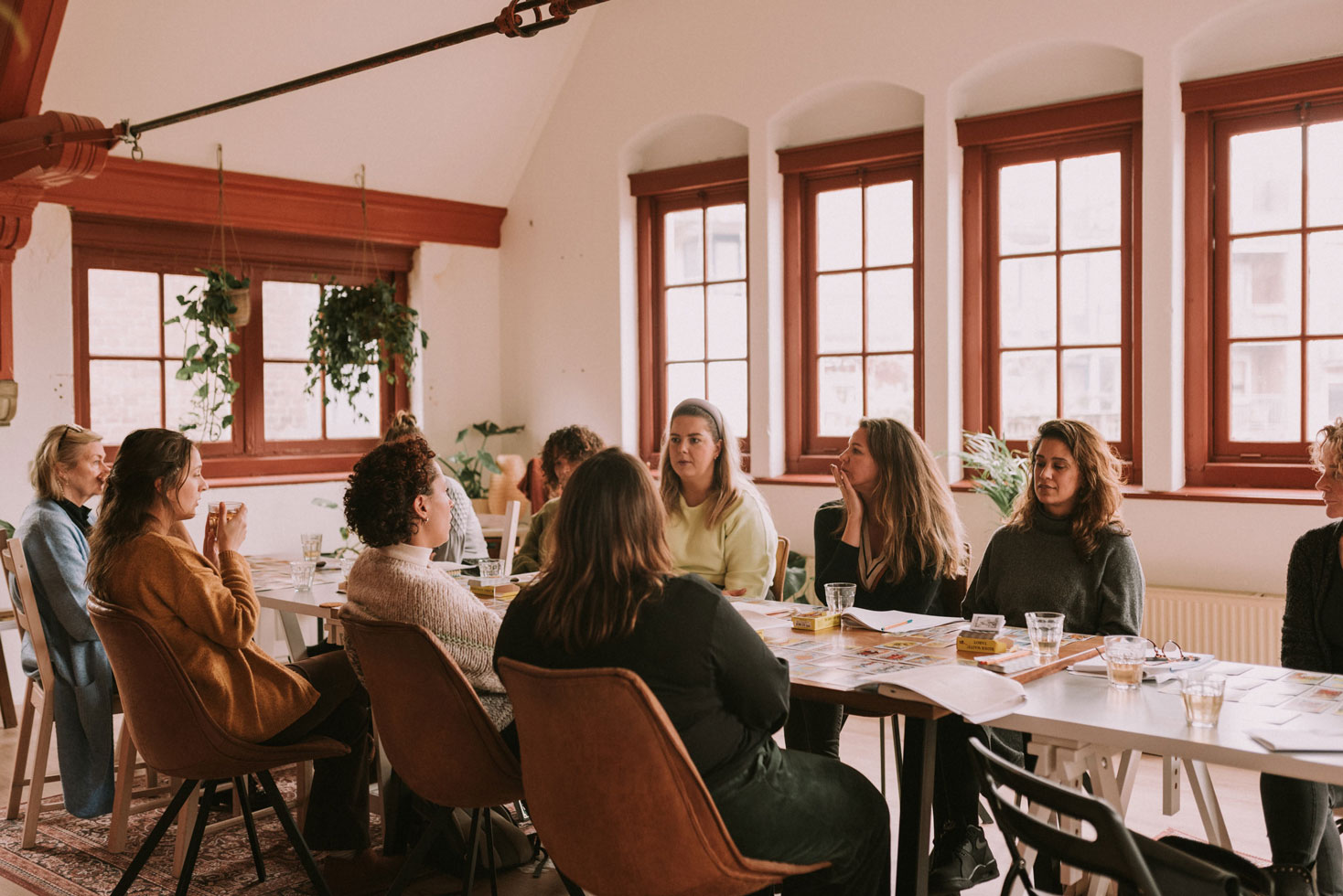 Group of women talking around a long table during a workshop in a loft with large red-framed windows