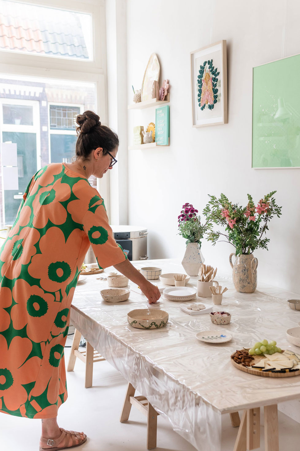 Host setting a table with handmade ceramics and fresh flowers before a workshop in a bright studio