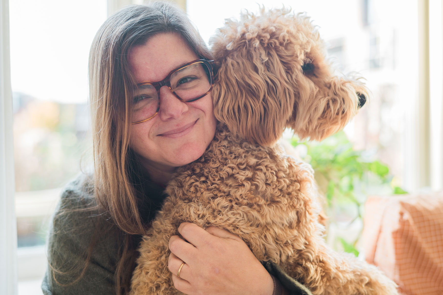 Pau Granillo, documentaire fotograaf in Haarlem, knuffelt thuis bij het raam haar krullende hond Hugo