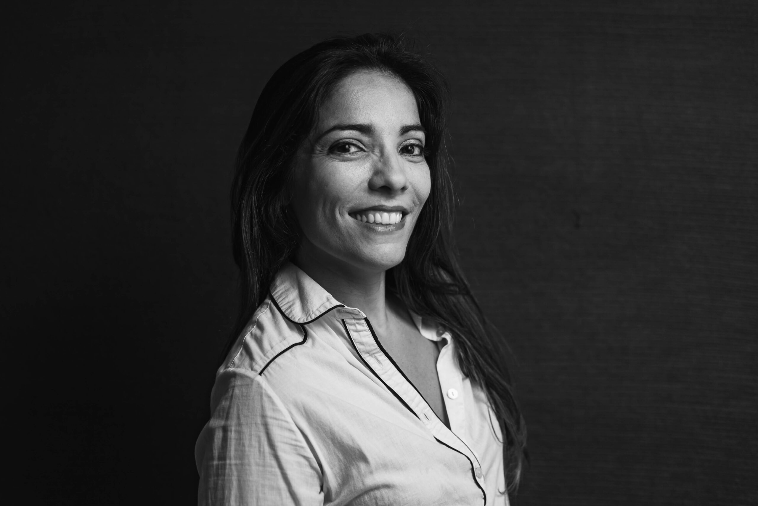Smiling woman in a white shirt, black and white headshot on a dark background, Headshot Day by Pau Granillo