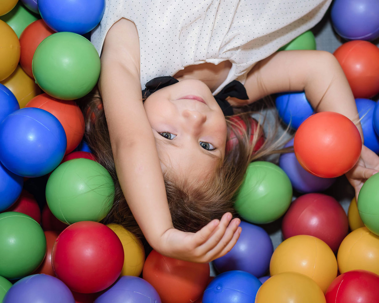 Little girl lying in a colourful ball pit, smiling up at the camera during a children's birthday party