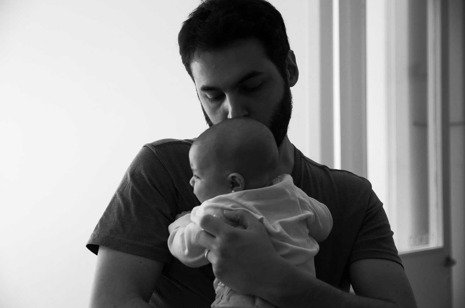 Dad kissing his baby's head by the window – newborn photographer Haarlem