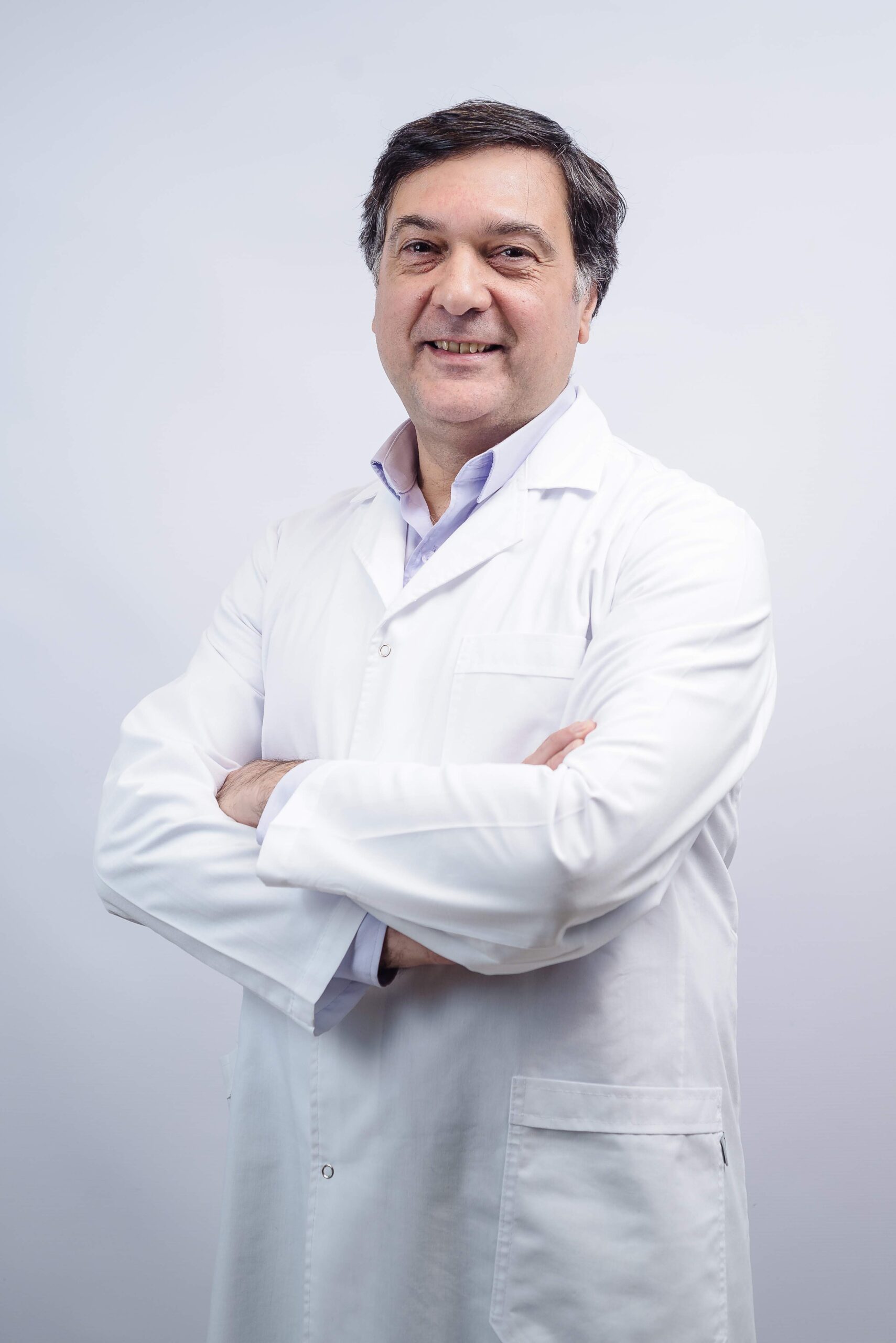 Smiling doctor in a white coat with arms crossed, professional headshot on a light background