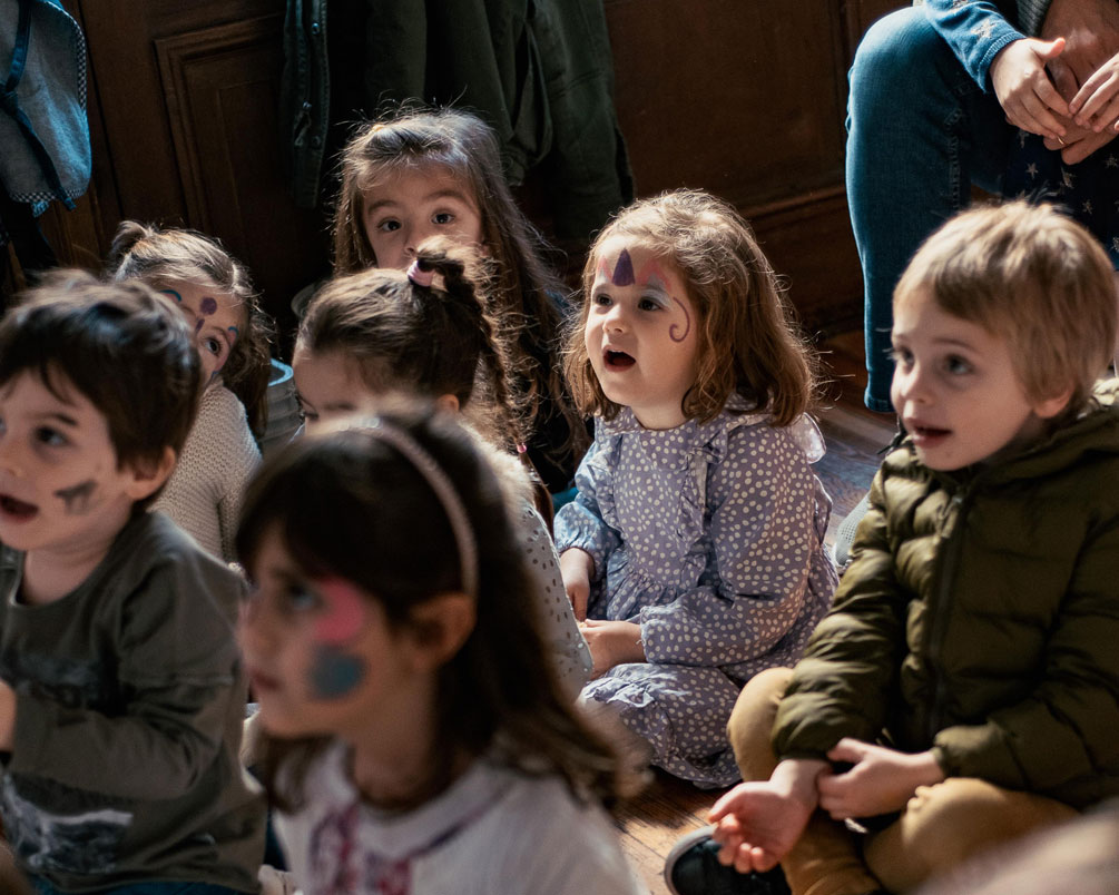 Group of children with painted faces sitting on the floor, watching a show at a birthday party