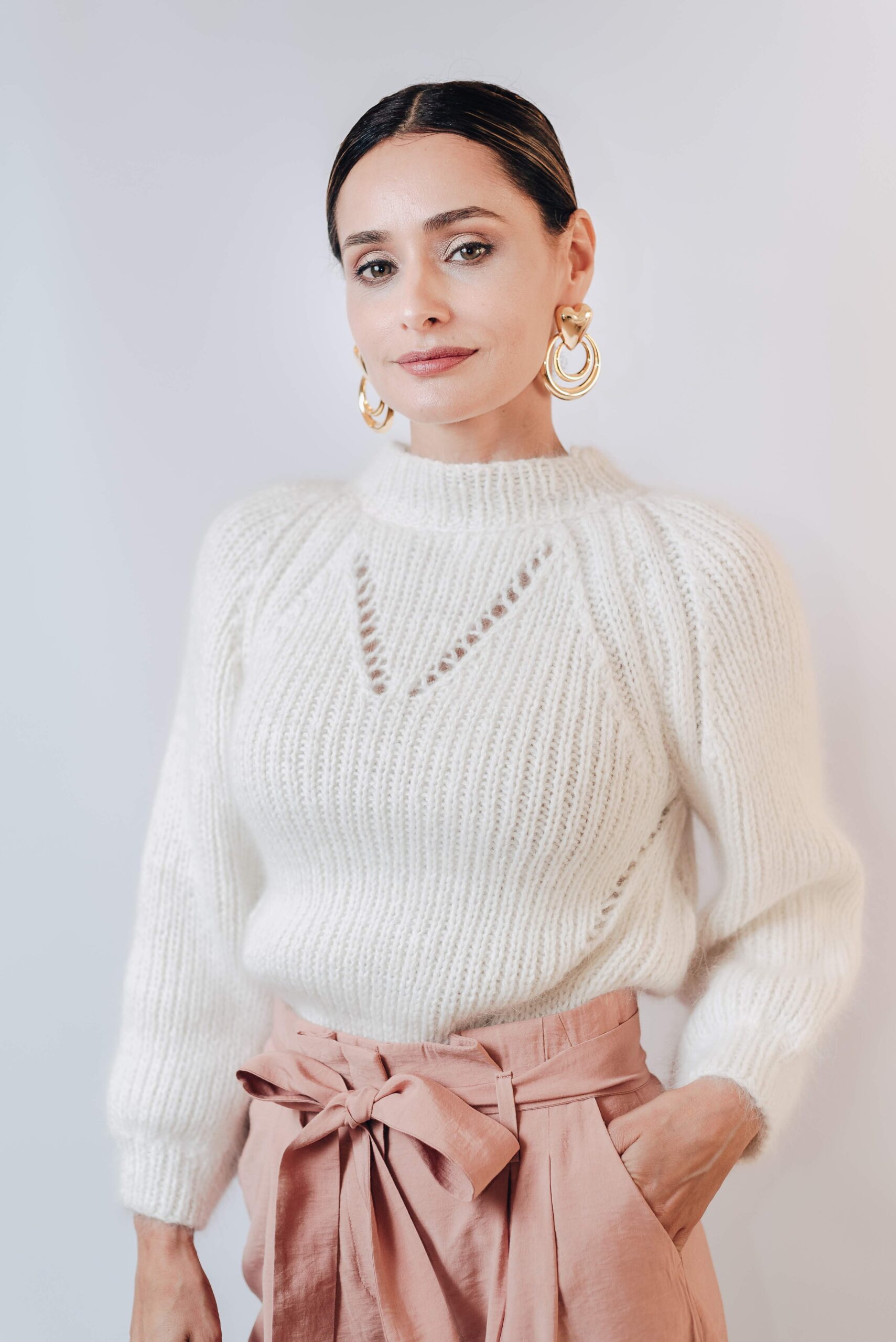 Woman in a white knit sweater and gold earrings, portrait on a light background