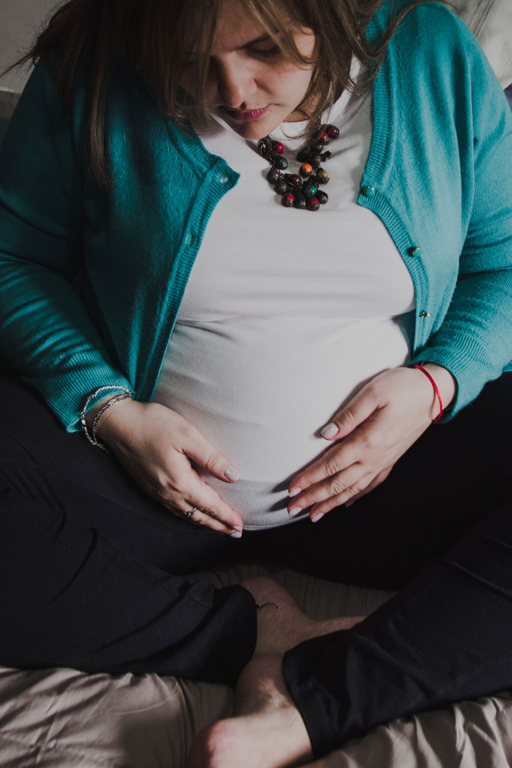 Pregnant woman sitting on the bed with her hands on her bump – maternity photos at home, Haarlem