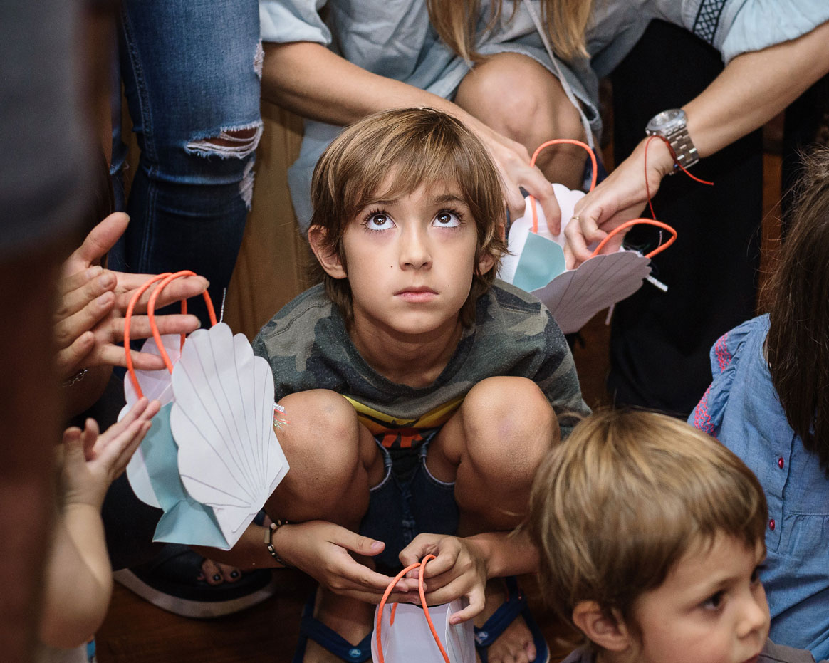 Boy crouching among guests and looking up in wonder at a children's party, family event photography