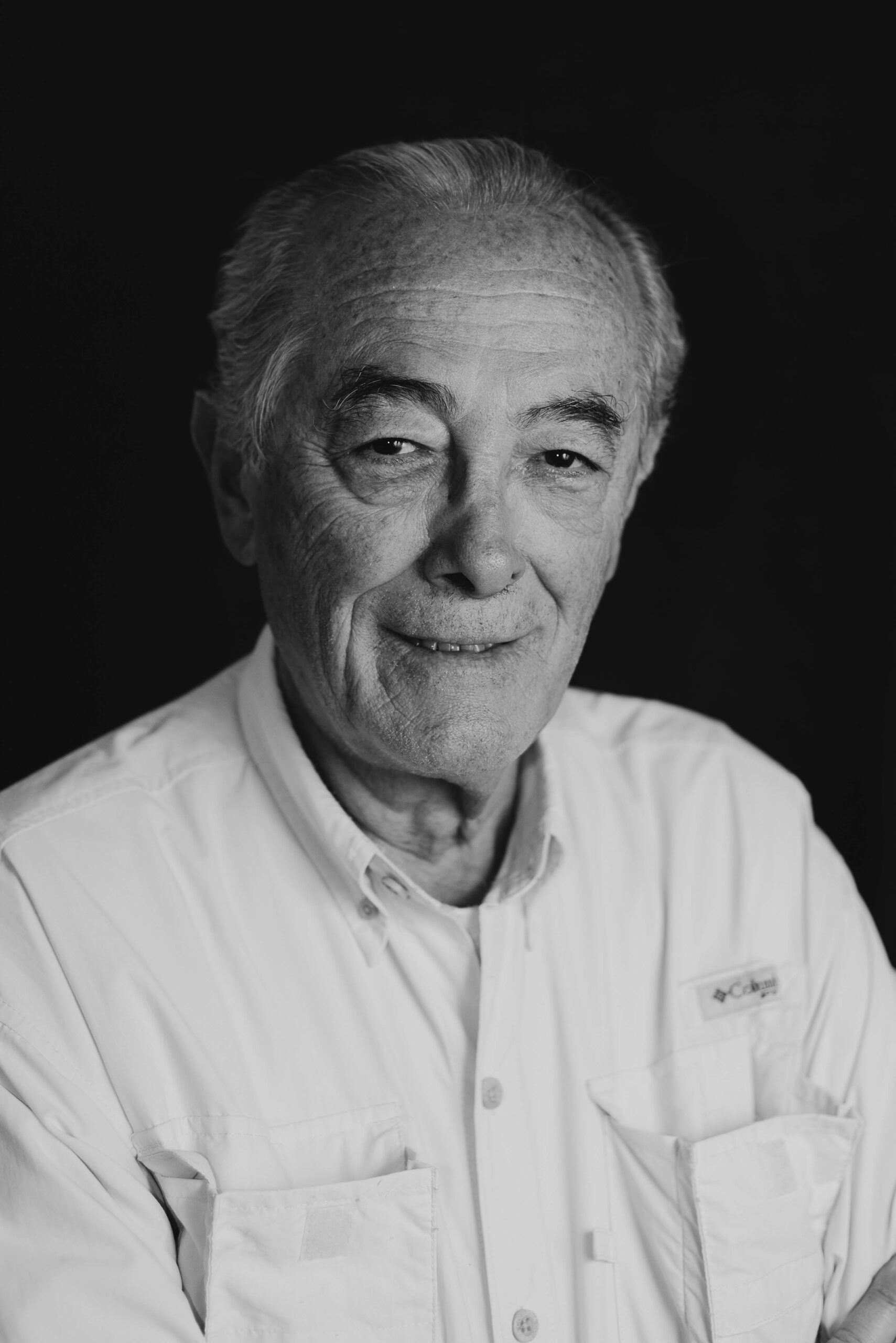Smiling older man in a white shirt, black and white headshot on a dark background