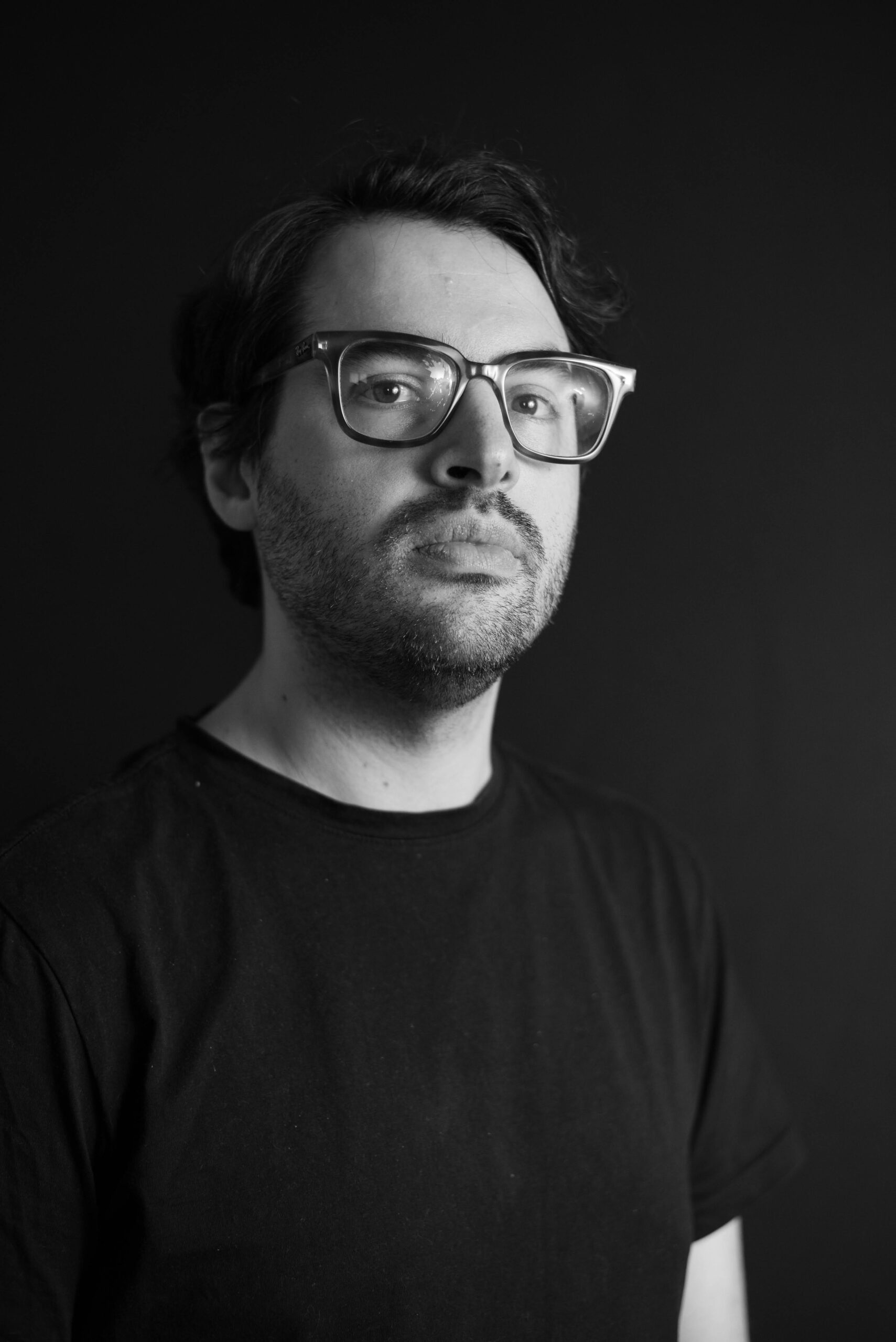 Man with glasses in a black T-shirt, black and white portrait on a dark background