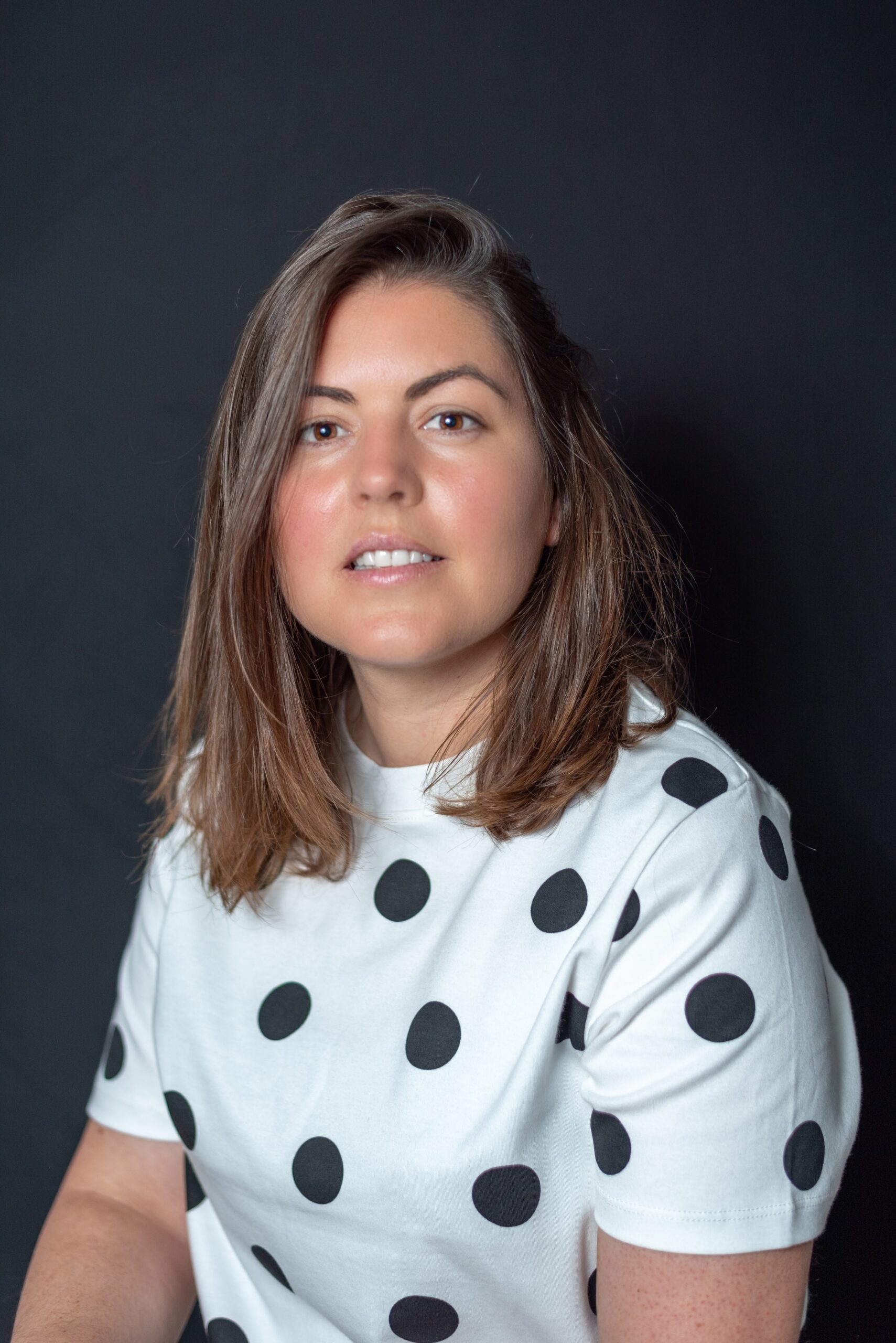 Woman in a polka dot T-shirt, colour headshot on a dark background