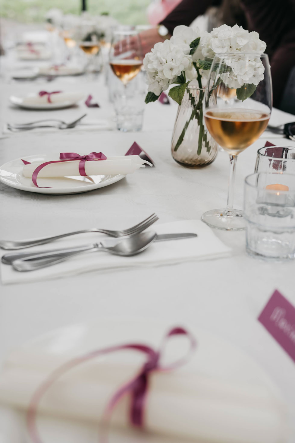 Rolled white napkin tied with a pink ribbon on a plate, event table detail