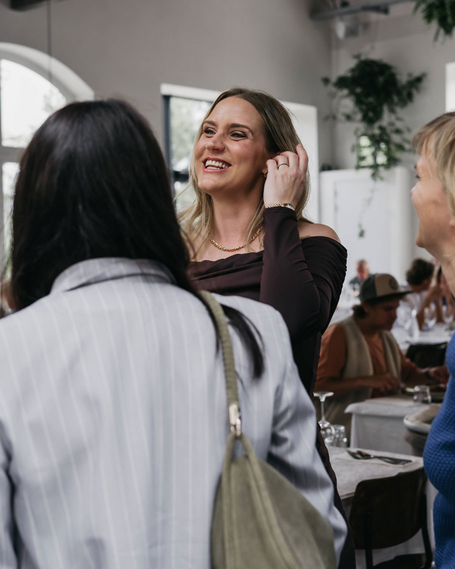 Women laughing and greeting each other around a long dinner table at a baby shower
