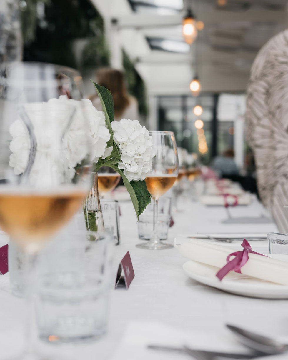 Long baby shower table with white hydrangeas, glasses of rosé and pink ribbons in a glass conservatory in Haarlem