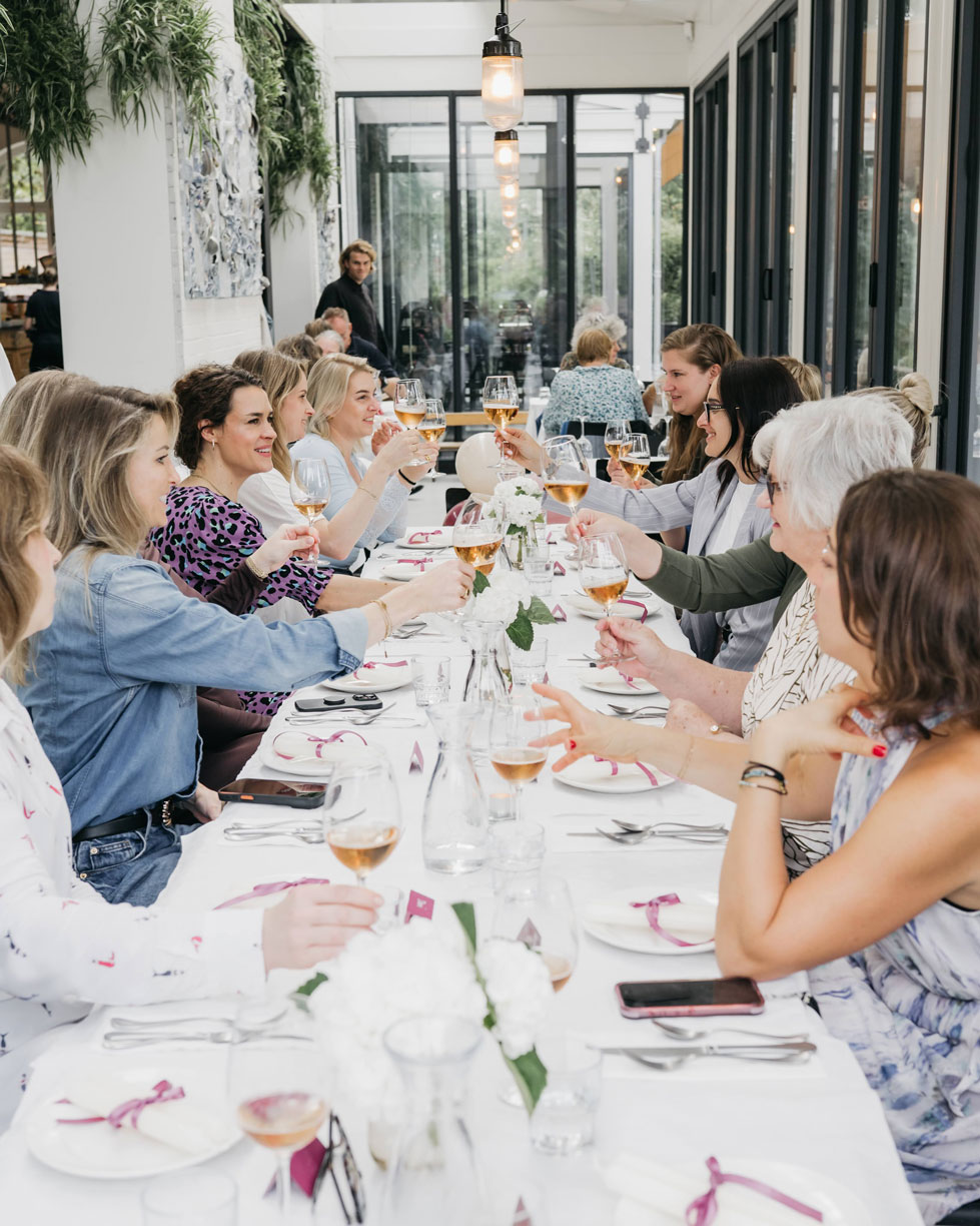 Guests raising their glasses in a toast along a long table in a bright glass conservatory
