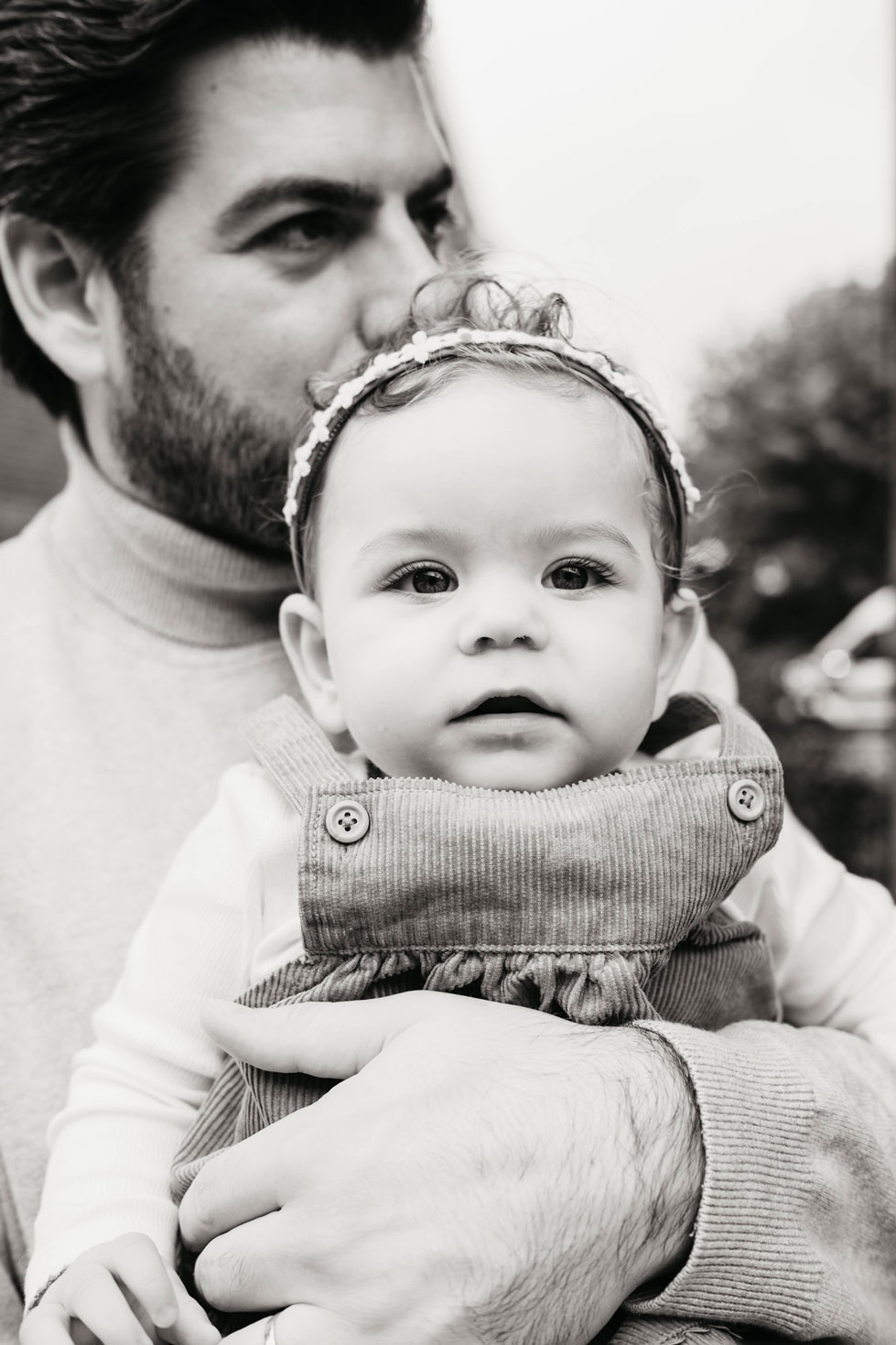 Black and white portrait of a baby with a flower headband, held by her father