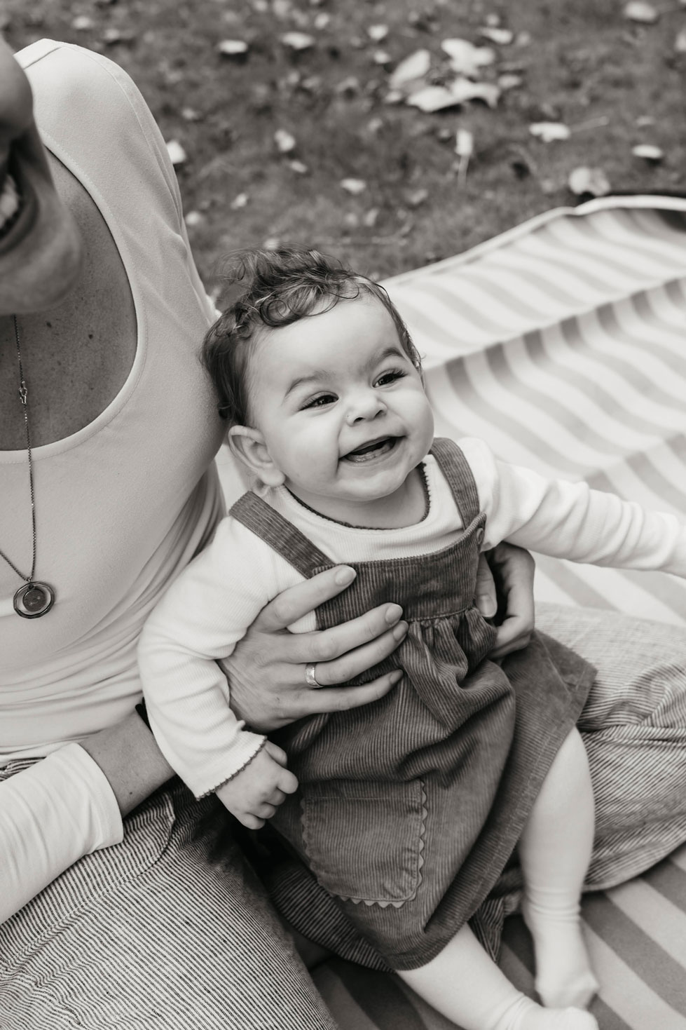 Smiling baby in a corduroy dress sitting on a striped picnic blanket in the park
