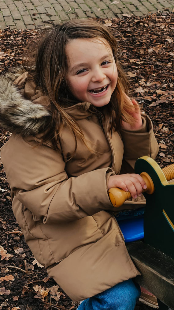 Laughing girl in a camel coat on a playground rocker during an autumn family photoshoot in Haarlem