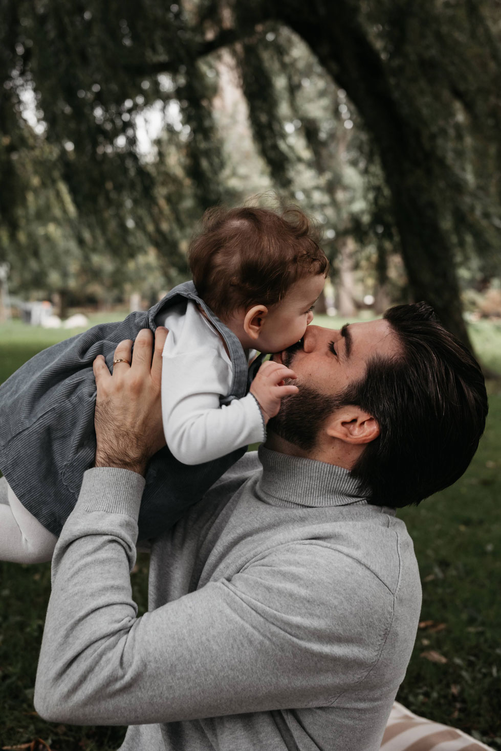 Father lifting his baby as she kisses his nose under a willow tree in Westerpark